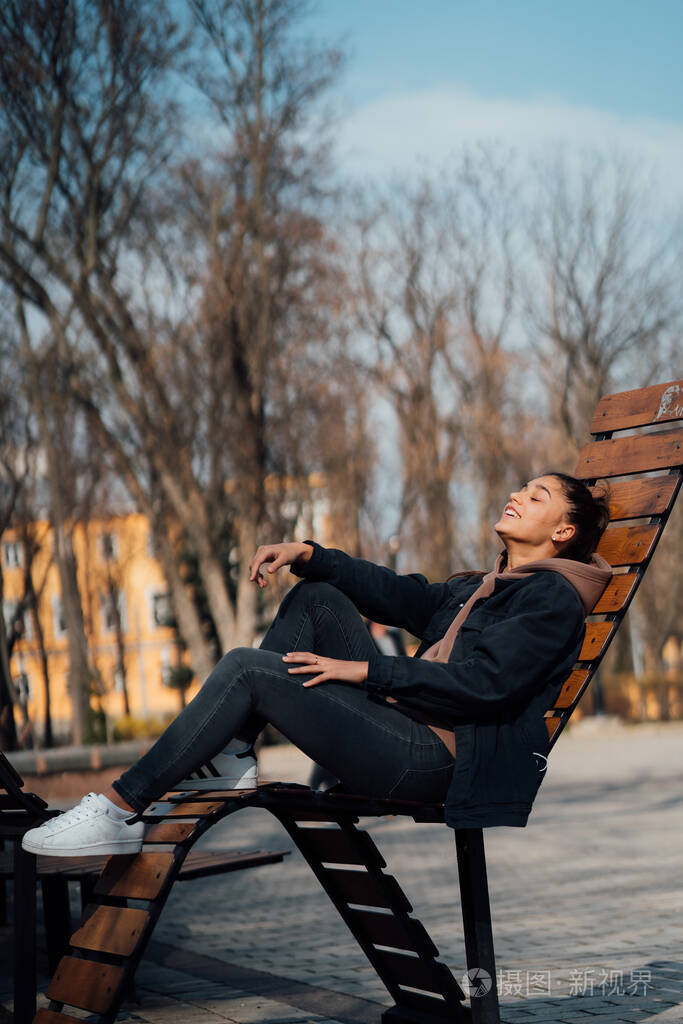 年轻女子坐在公园的长椅上微笑着看着镜头