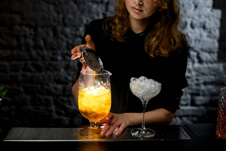 女酒吧男侍者用鸡尾酒把滤网举过玻璃杯。