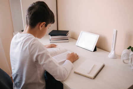小男孩坐在书桌旁看书.检疫期间在家学习照片