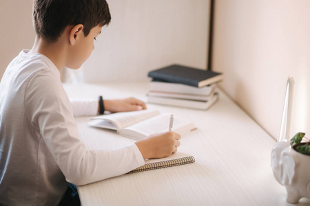 坐在书桌旁的小男孩读了这本书，并把它记在笔记本上。检疫期间在家学习