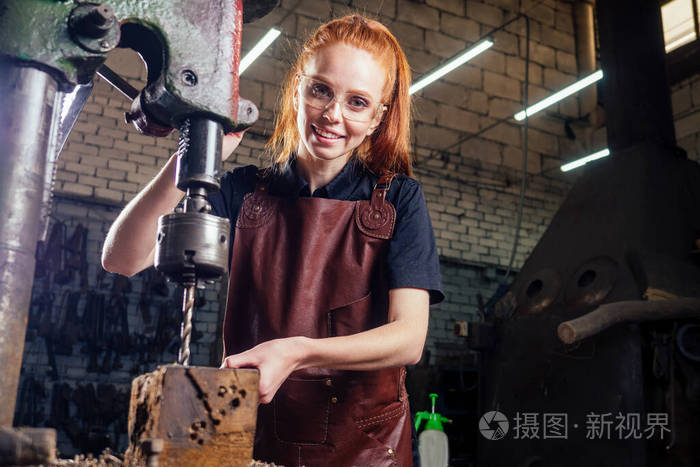 红发姜黄色的年轻欧洲女权主义者穿着皮围裙在做铁匠小作坊业务强大