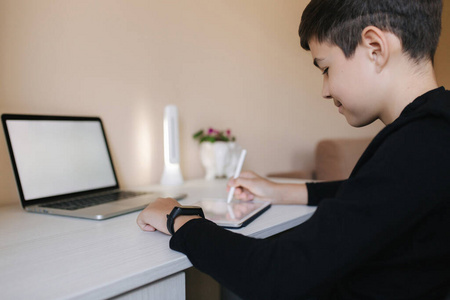 英俊的小男孩在家里画画。十几岁的男孩上班用平板电脑。小学生在家里用平板电脑笔记本电脑智能手机学习