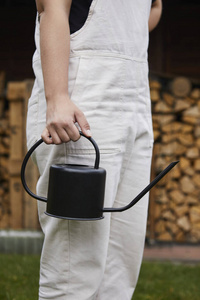 一个穿着鲜艳工装裤的年轻园丁手里拿着一个黑色的水壶.