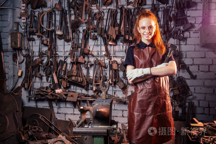 红发姜黄色的年轻欧洲女权主义者穿着皮围裙在做铁匠小作坊业务强大