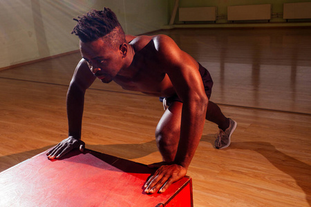 晚上在昏暗的健身房里，一个非洲男人在地板上推着