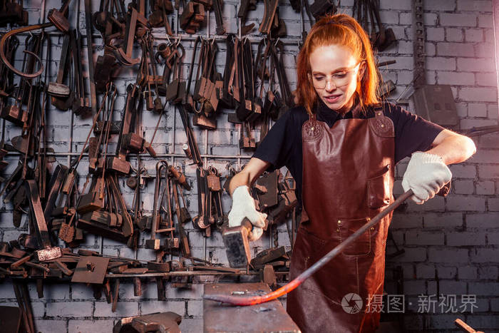 红发姜黄色的年轻欧洲女权主义者,穿着皮围裙在做铁匠小作坊业务强大