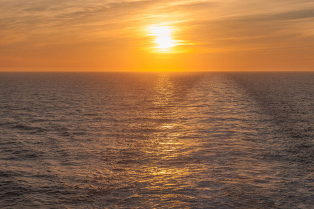 日落在海上，你可以看到游轮留下的尾流