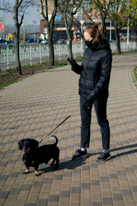 冠状病毒。冠状病毒感染期间，戴着面罩和橡胶手套的年轻白人妇女带着他的狗在家附近散步。covid19大流行期间的短距离步行。