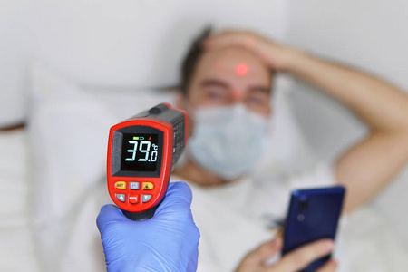 用非接触式体温计测量男性体温。在病房里戴着防护面罩的病人。