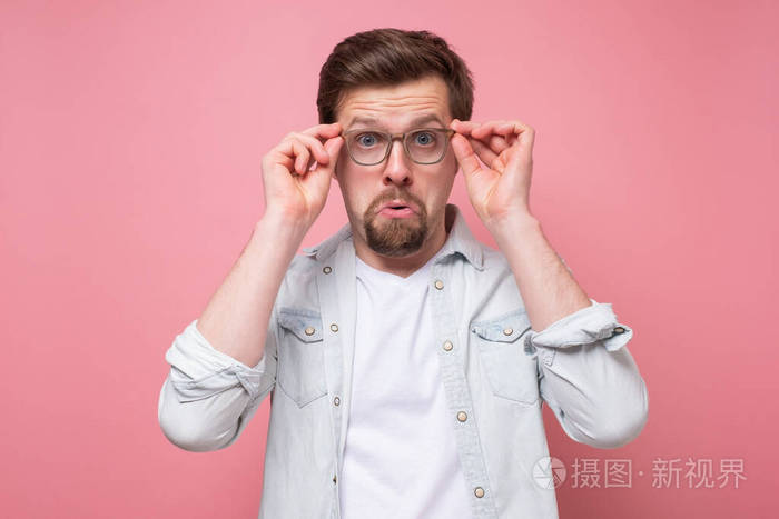 惊讶的白人年轻人透过眼镜看着相机