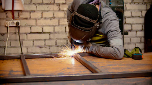 戴着防护帽的工人在焊接金属梁之间的接缝