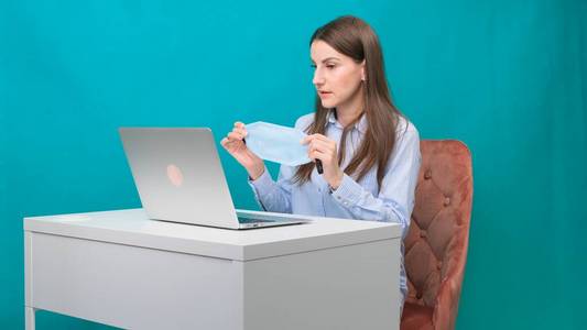 大流行期间，女性在工作场所或家中使用笔记本电脑时戴上防护面具。隔离隔离期间的工作理念。