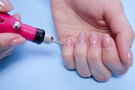 在一个手指上做一个美丽的指甲的过程在一个蓝色背景的指甲美容院用一个特殊的机器加工一个指甲