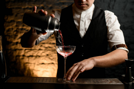 特写专业调酒师将鸡尾酒从不锈钢摇壶倒入玻璃杯