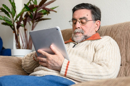 一位老人坐在沙发上，在客厅里使用数码平板电脑。