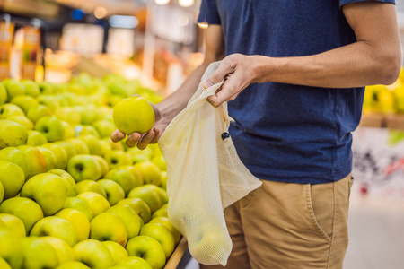 男人在超市里不使用塑料袋挑选苹果。可重复使用的蔬菜袋。零浪费理念