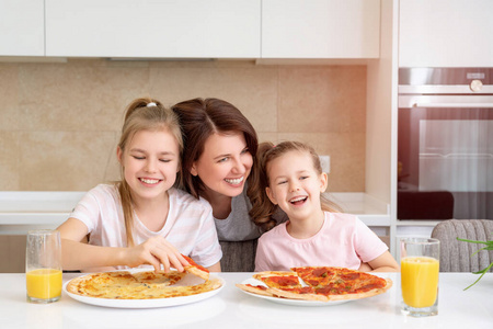 妈妈和两个女儿在厨房的桌子上吃自制比萨饼，快乐的家庭观念