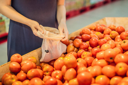 一位妇女在超市挑选西红柿时没有使用塑料袋。可重复使用的蔬菜袋。零浪费理念