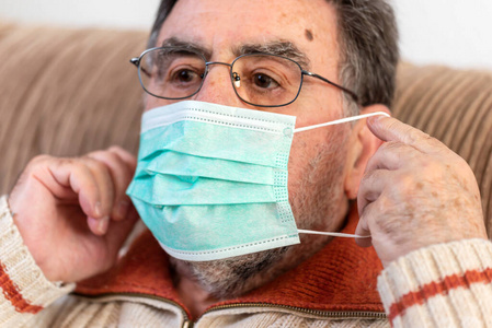 Elderly man putting a medical mask on his face to protect himsel