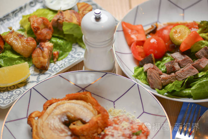 肉和蔬菜沙拉。意大利料理，餐厅里供应的不同菜肴都放在浅色的乡村木桌上。