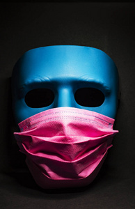 Medical pink mask put on a blue mask. black background
