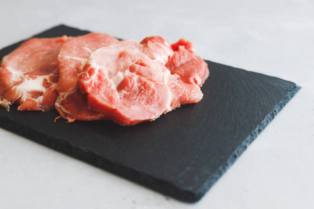 生鲜猪肉堆不会躺在灰色背景的黑色石板上。节省空间。肉类加工