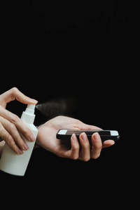 男性手用消毒喷雾消毒智能手机表面的黑色背景。Covid19冠状病毒检疫大流行。在家里与世隔绝。保护你自己和你爱的人。