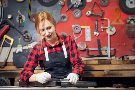 年轻漂亮的女工匠工程师站在围裙上,站在手工工具的背景上.