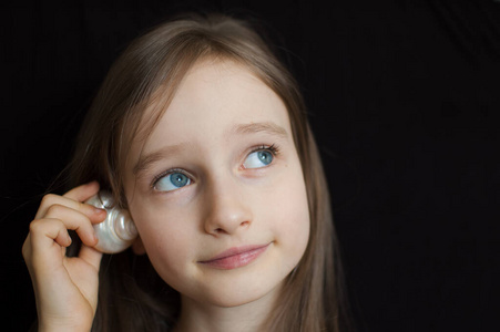 贝壳的旁边可爱的金发女孩微笑着拿着贝壳在她的耳朵旁边,听在黑色