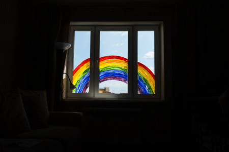 科维德19在家隔离期间画彩虹。靠近窗户的女孩。为预防冠状病毒呆在家里的社交媒体运动，让大家都好起来，希望在冠状病毒大流行期间有