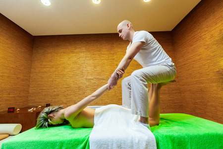 在spa沙龙，按摩师拉着女人的手臂在做传统的泰式按摩。美容治疗理念