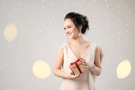 一个年轻的黑发女人，穿着晚礼服，背景是白色。拿着圣诞礼物盒。快乐，快乐和惊喜。