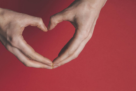 Female hands creating the shape of a heart over a red background