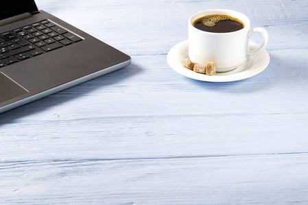 在浅蓝色的旧木桌上放着一杯咖啡的笔记本电脑。带一杯新鲜咖啡的笔记本。在家工作概念