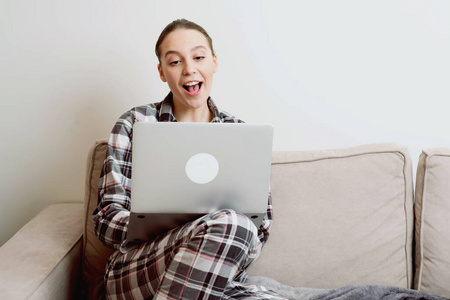 一个穿着睡衣坐在家里沙发上的女孩用一台笔记本电脑，正在寻找隔离区的工作。