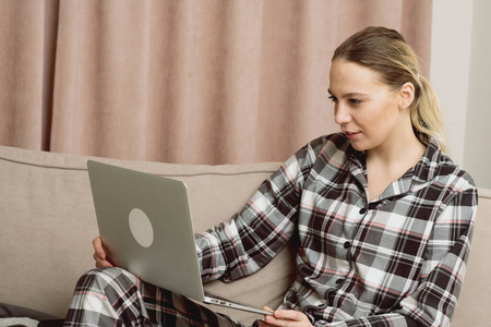 一个年轻漂亮的女孩穿着睡衣坐在沙发上，在隔离期间在网上找工作。