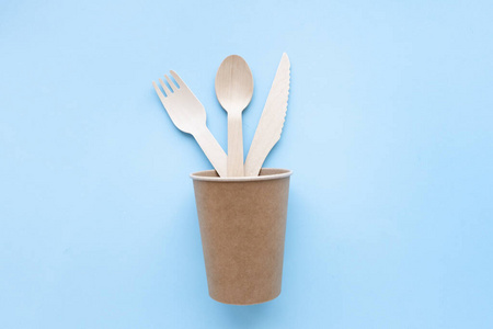 蓝色背景的环保一次性厨房用具。纸杯里的木制叉子和勺子。生态，零浪费理念。俯视图。平铺