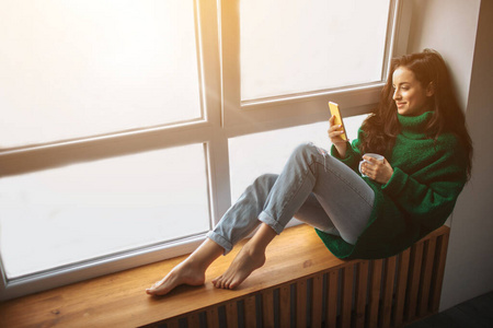 穿绿色毛衣的女模特坐在窗边向外看照片