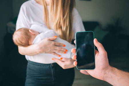 一个年轻家庭的智能手机应用程序。母亲抱着一个新生儿。爸爸把手机屏幕对着摄像机