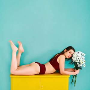 一个穿着运动服的年轻女孩躺在一个黄色的五斗橱里，手里拿着花