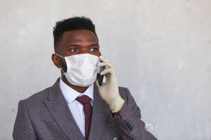 科维德19穿着西装的英俊的非洲黑人男子戴着医用面罩手戴手套拿着手机