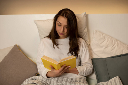 一个黑发女孩，穿着睡衣，坐在床上看书