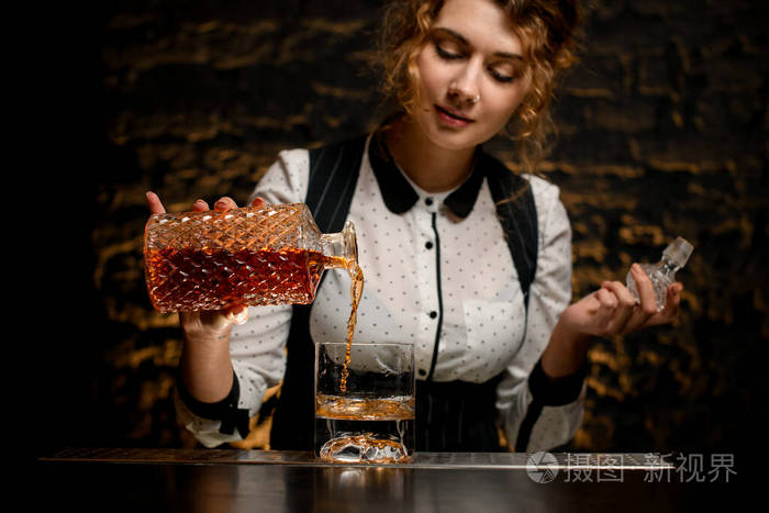 女调酒师准确地将酒精饮料从酒瓶倒入玻璃杯