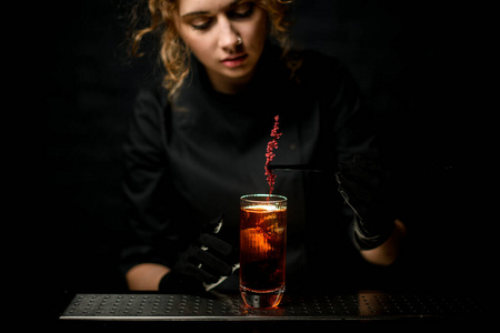 年轻的女酒保用花枝整齐地装饰鸡尾酒杯