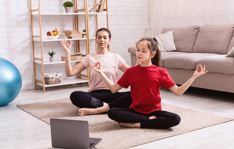 家庭体育。母女俩一边练瑜伽，一边在笔记本电脑上看在线教程