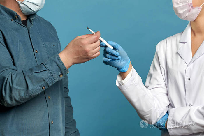 年轻的医生用体温计测量病人的体温摄影棚在蓝色背景下拍摄