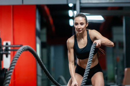 一个有魅力的年轻肌肉女孩在健身房里用训练绳锻炼