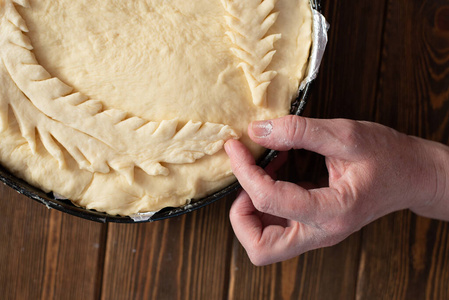 a raw pie with cabbage lies on a wooden table. human hands decor