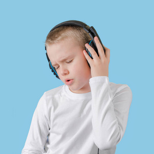 小孩子把手放在耳机上，享受听音乐和唱歌的乐趣。戴着耳机的男孩。