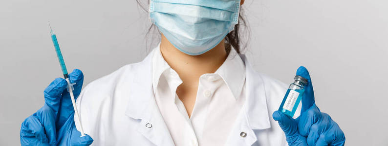 医生，传染病学家，研究和covid19概念。亚洲女护士特写，戴着医用口罩手套和白大褂，手持注射器和装有冠状病毒疫苗的安瓿，为人